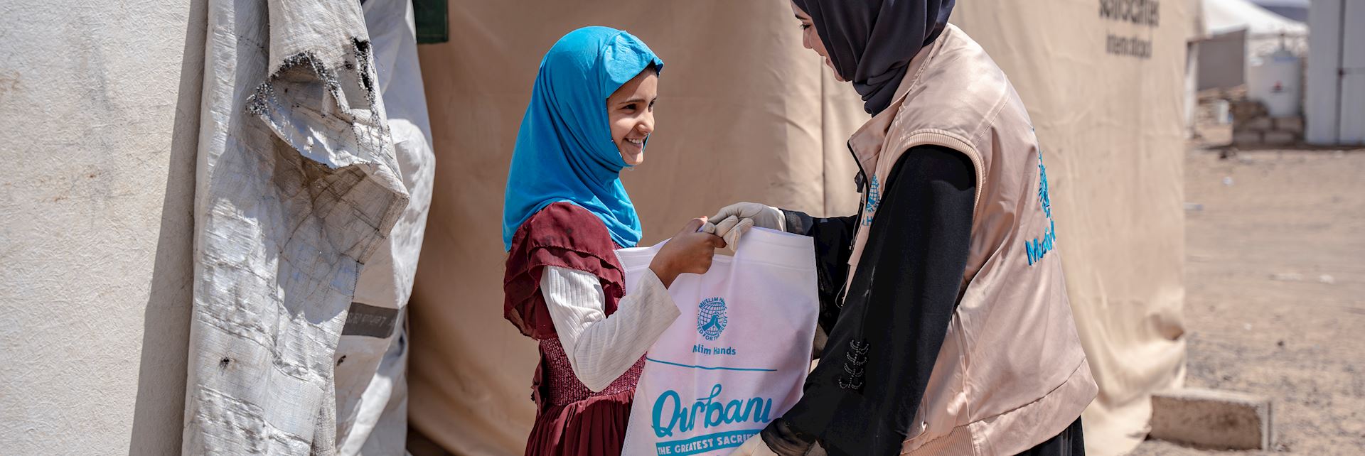 Une humanitaire de Muslim Hands remet un colis de viande de sacrifice à une jeune fille.